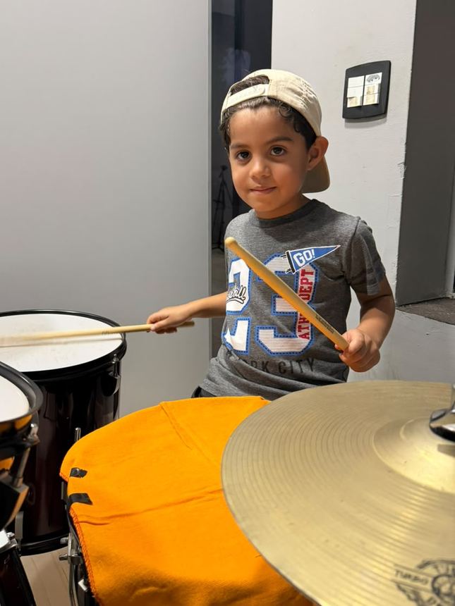 Menino de boné tocando bateria na sala da escola