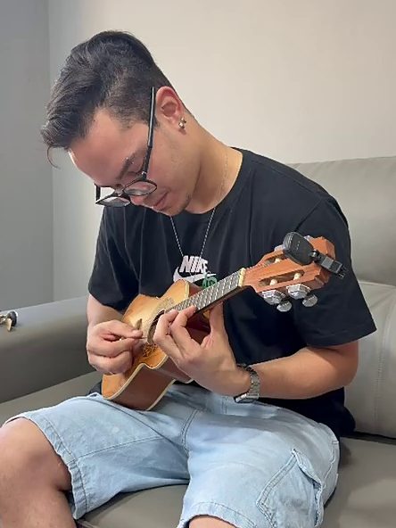 Jovem de óculos tocando ukulele sentado no sofá da sala