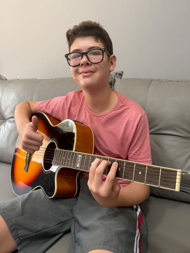 Adolescente de óculos tocando violão no sofá da sala